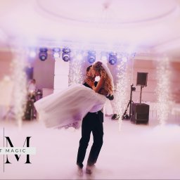 4LClover Aleksander Gacek - Mężczyzna trzyma Pannę Młodą na tle dekoracji pirotechnicznych i oświetlenia scenicznego w sali balowej. Romantyczny taniec pary młodej.