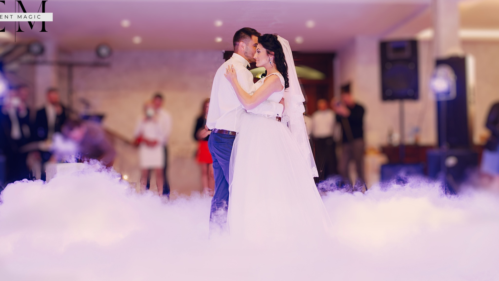 Para młoda tańczy pierwszy taniec we mgle, w tle widoczni goście i sprzęt nagłośnieniowy.