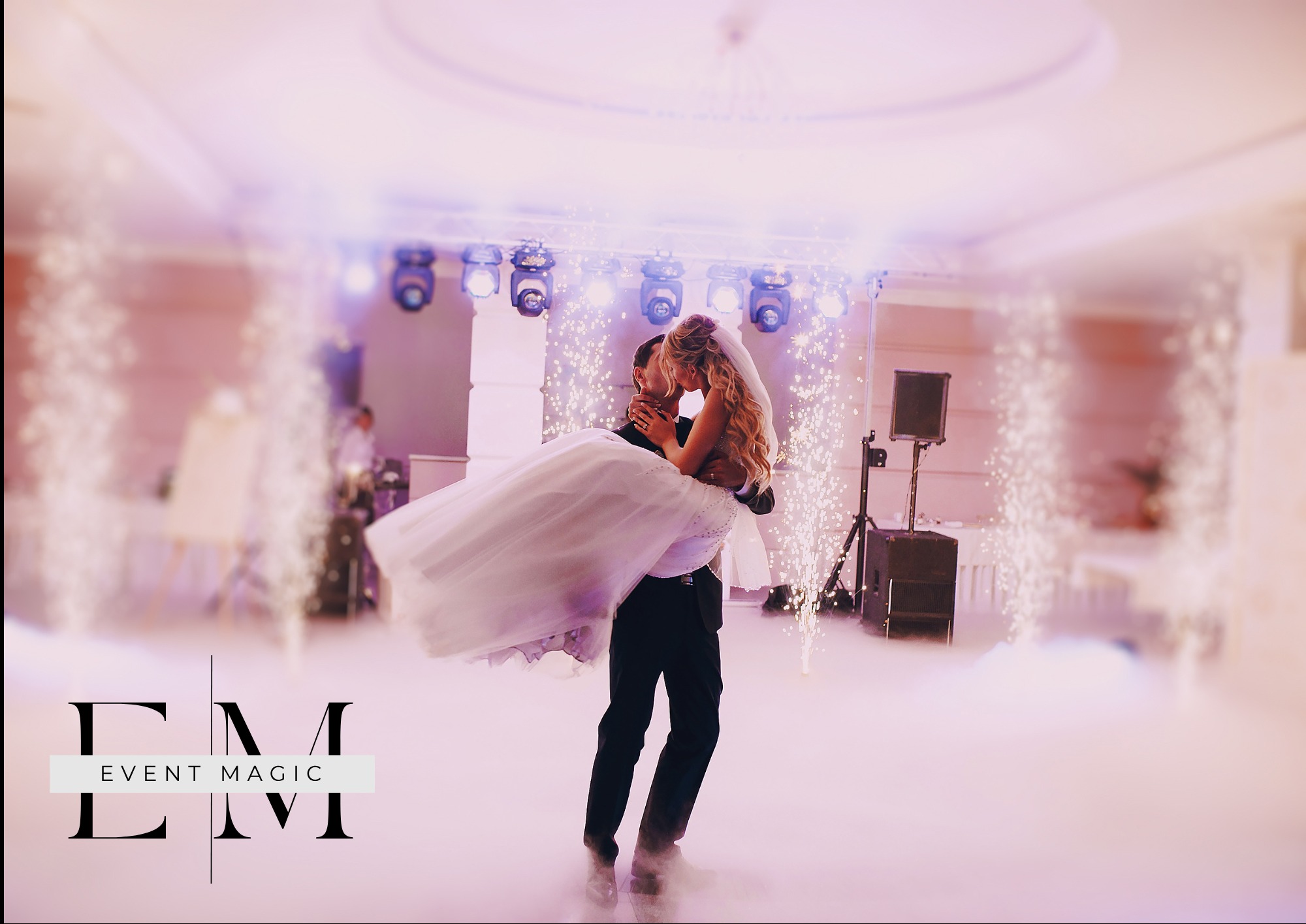 Mężczyzna trzyma Pannę Młodą na tle dekoracji pirotechnicznych i oświetlenia scenicznego w sali balowej. Romantyczny taniec pary młodej.
