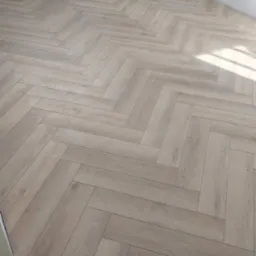 Ułożone panele podłogowe w jodełkę, z zachowanymi odstępami przy ścianach, zabezpieczonymi żółtymi klinami dystansowymi.