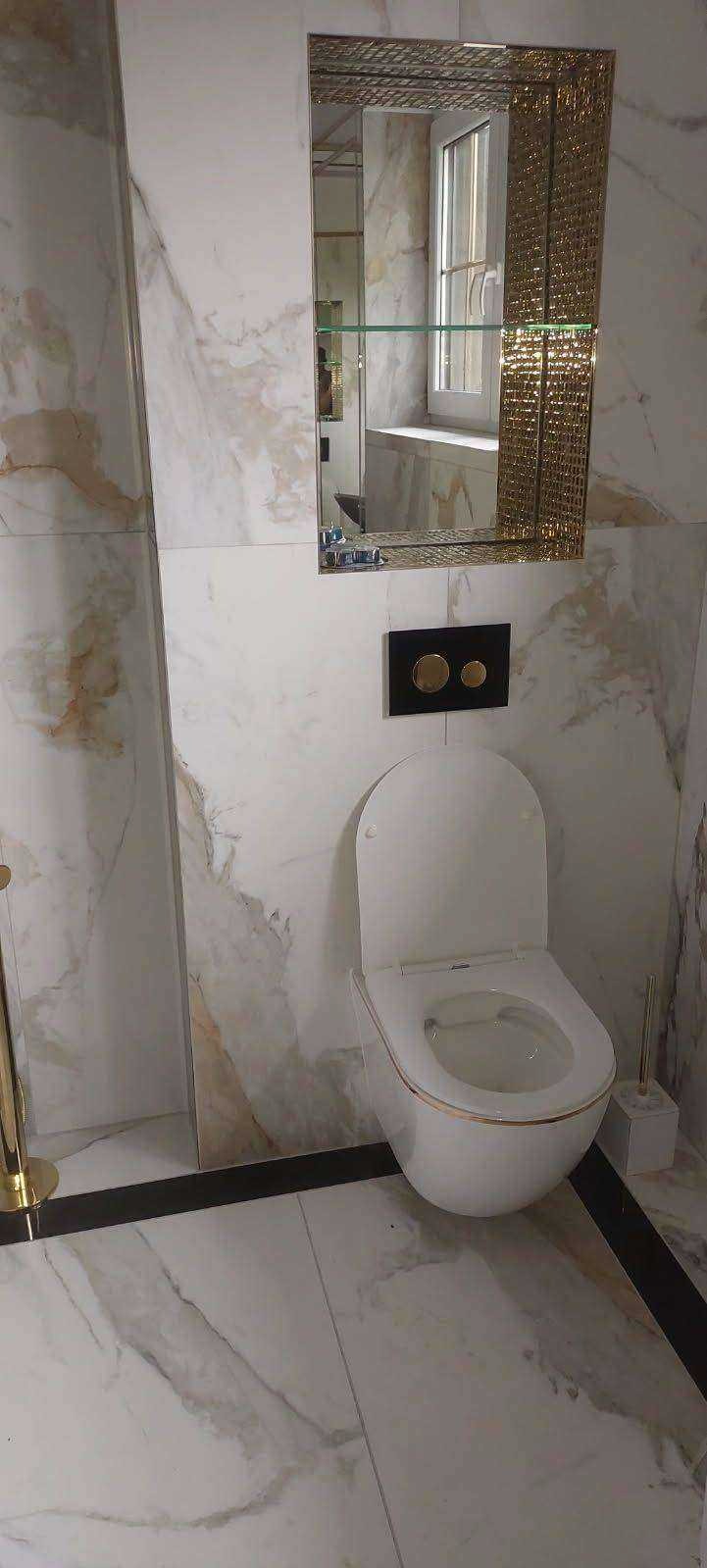 Elegancka toaleta wisząca w łazience z marmurowymi płytkami, złote akcenty na armaturze i lustrze z dekoracyjną ramą.