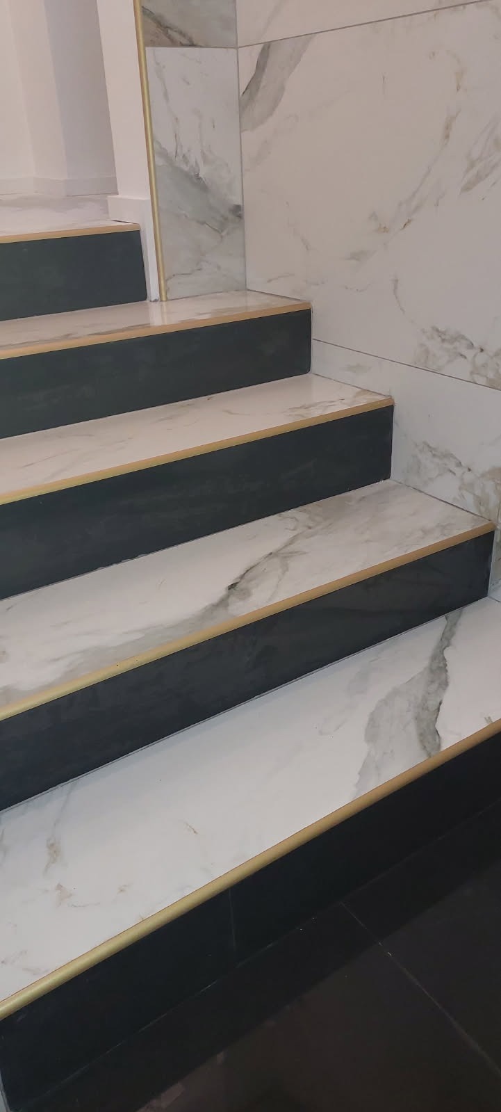 Wykończone schody z płytek imitujących marmur, z czarnymi podstopnicami i złotymi listwami krawędziowymi.