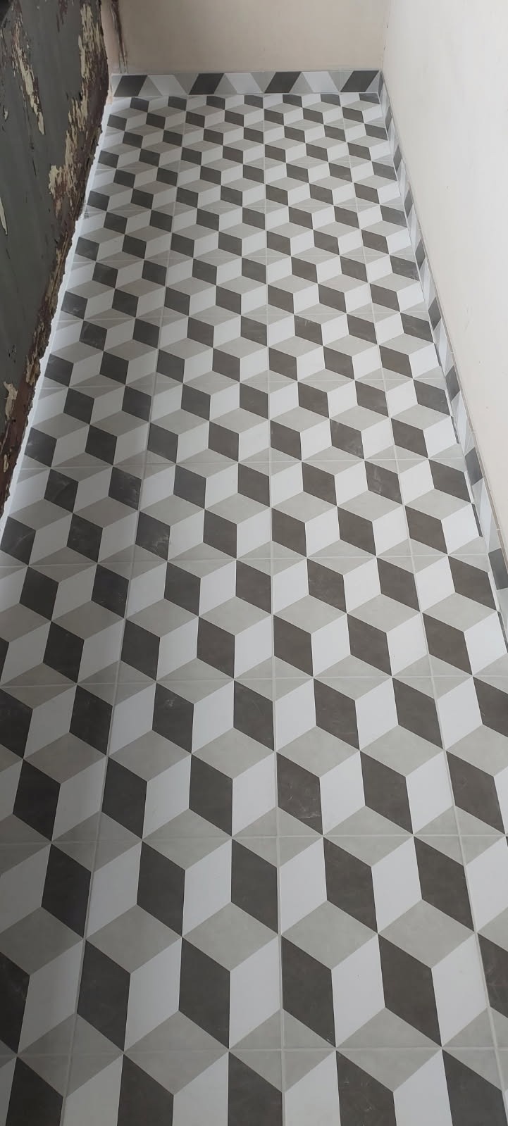 Ułożona podłoga z płytek w geometryczny wzór 3D, szare, białe i grafitowe kostki, widoczna ściana w trakcie remontu.