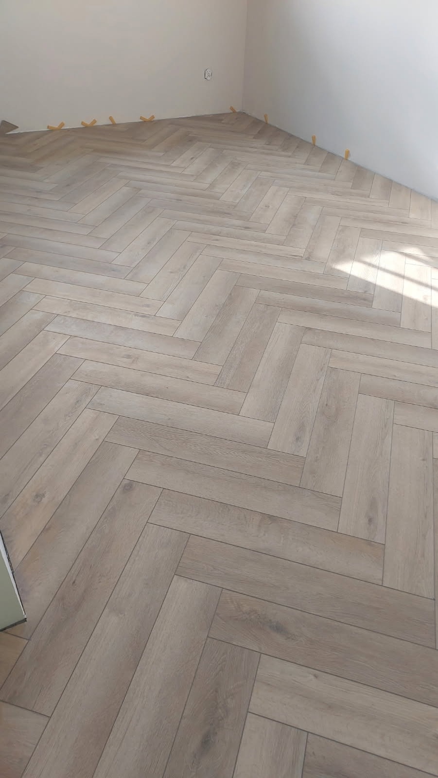 Ułożone panele podłogowe w jodełkę, z zachowanymi odstępami przy ścianach, zabezpieczonymi żółtymi klinami dystansowymi.