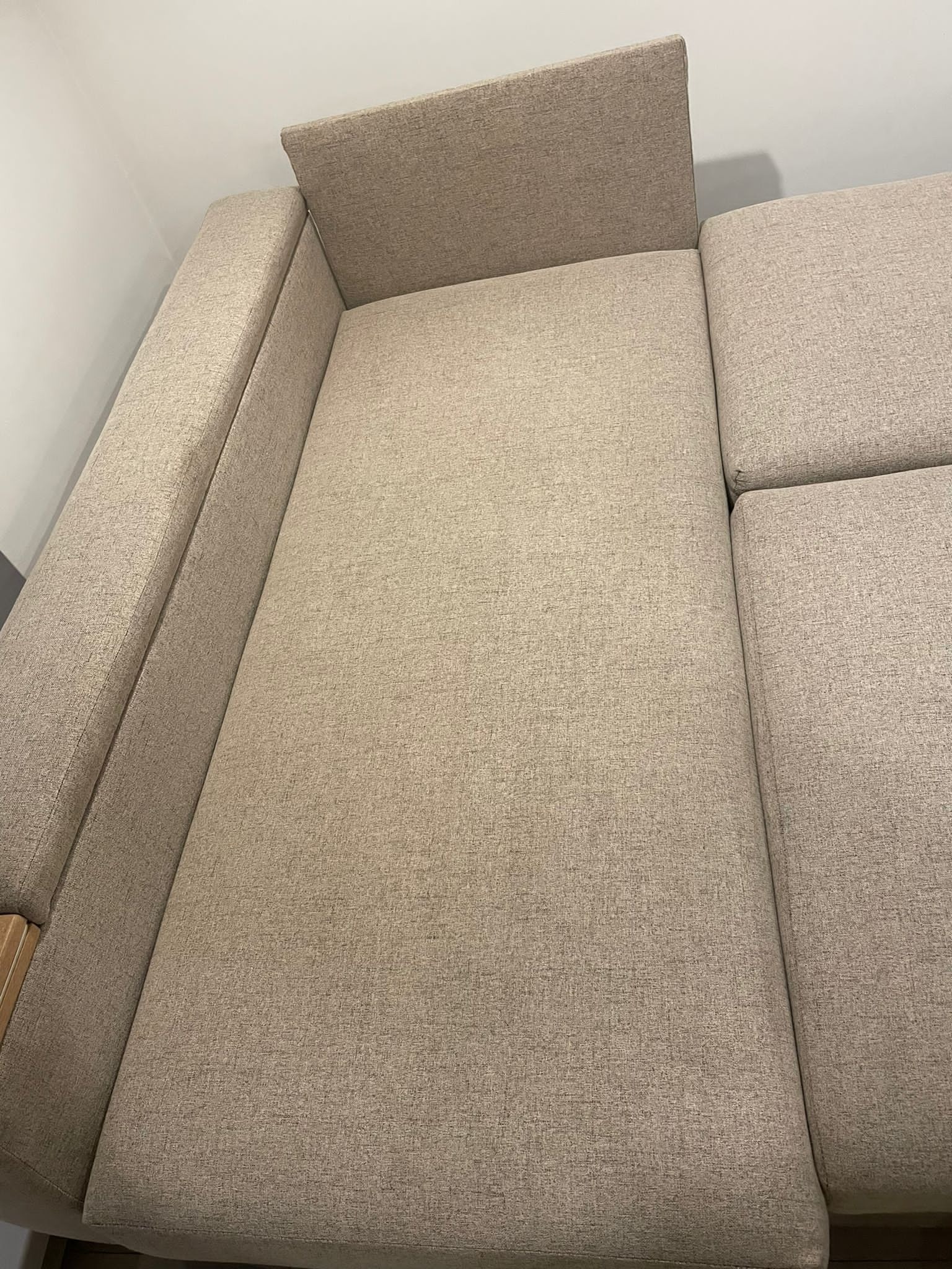 Fragment beżowej, tekstylnej sofy modułowej z widoczną fakturą materiału i drewnianym elementem podłokietnika.