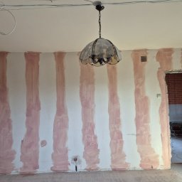 ARKADIUSZ Grzegorz Płatek - Pokój w trakcie przygotowania do malowania: ściany z pionowymi pasami zagruntowane, widoczna instalacja elektryczna na suficie, wisząca lampa i fragment sąsiedniego pomieszczenia z instalacją...