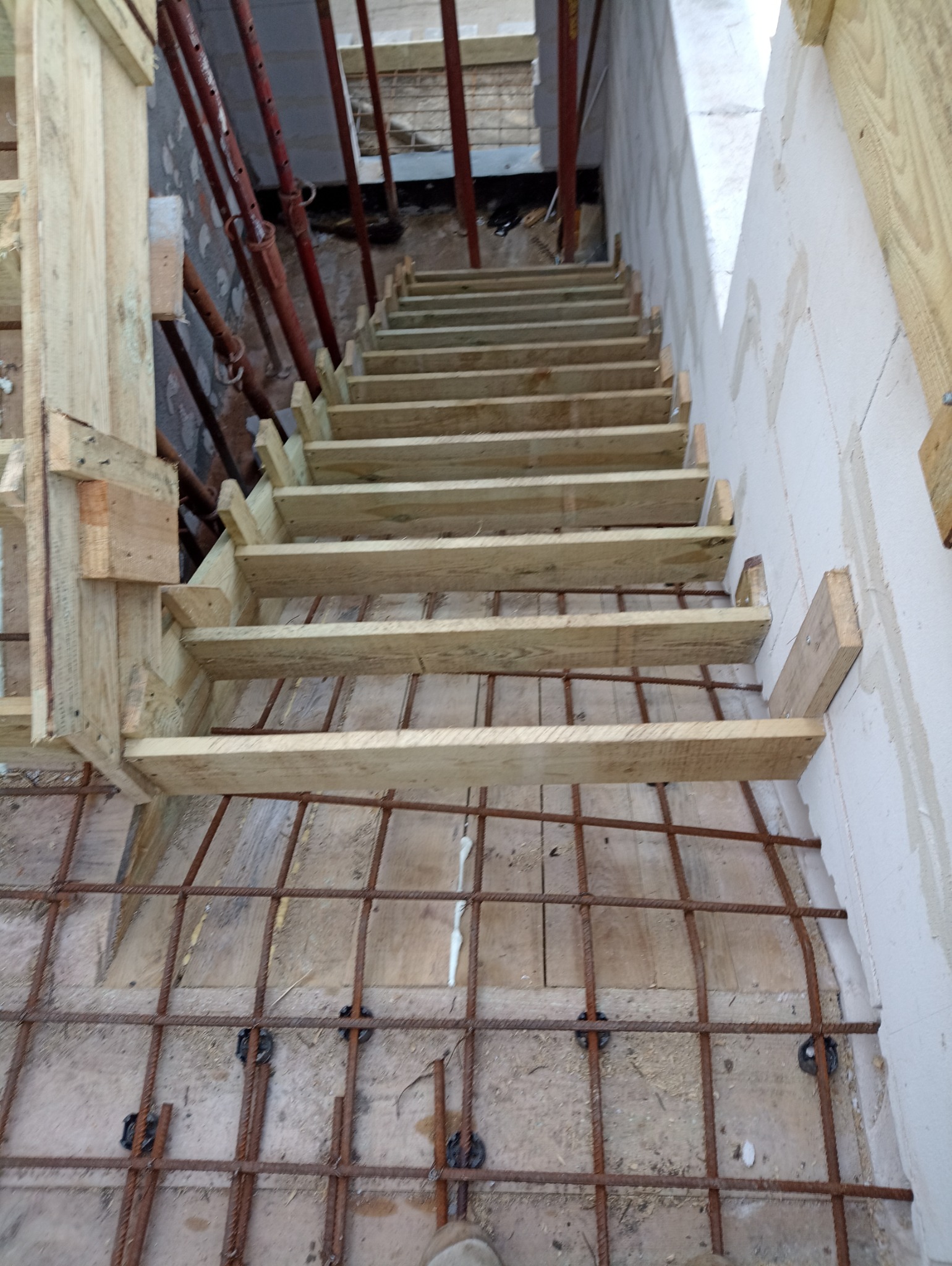 Szkielet drewnianych schodów w trakcie budowy, widoczne stalowe podpory, zbrojenie pod wylewkę betonową i ściana z betonu komórkowego.