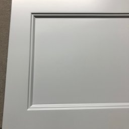 MEB-LAK - Szary front meblowy z frezowanym obramowaniem, leżący na szorstkiej powierzchni. Detal wykończenia szafki lub szuflady w zbliżeniu.