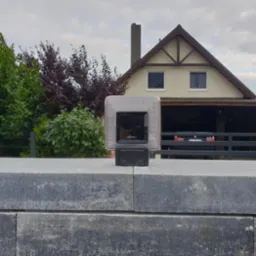 Fotokomórka FAAC zamontowana na szarym, kamiennym słupku bramy wjazdowej, na tle domu z garażem i zielenią.