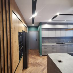 Lutsyk - Nowoczesna kuchnia po remoncie: drewniane lamele na zabudowie, szara zabudowa kuchenna z marmurowym backsplash, parkiet w jodełkę, wyspa kuchenna z szarego kamienia.