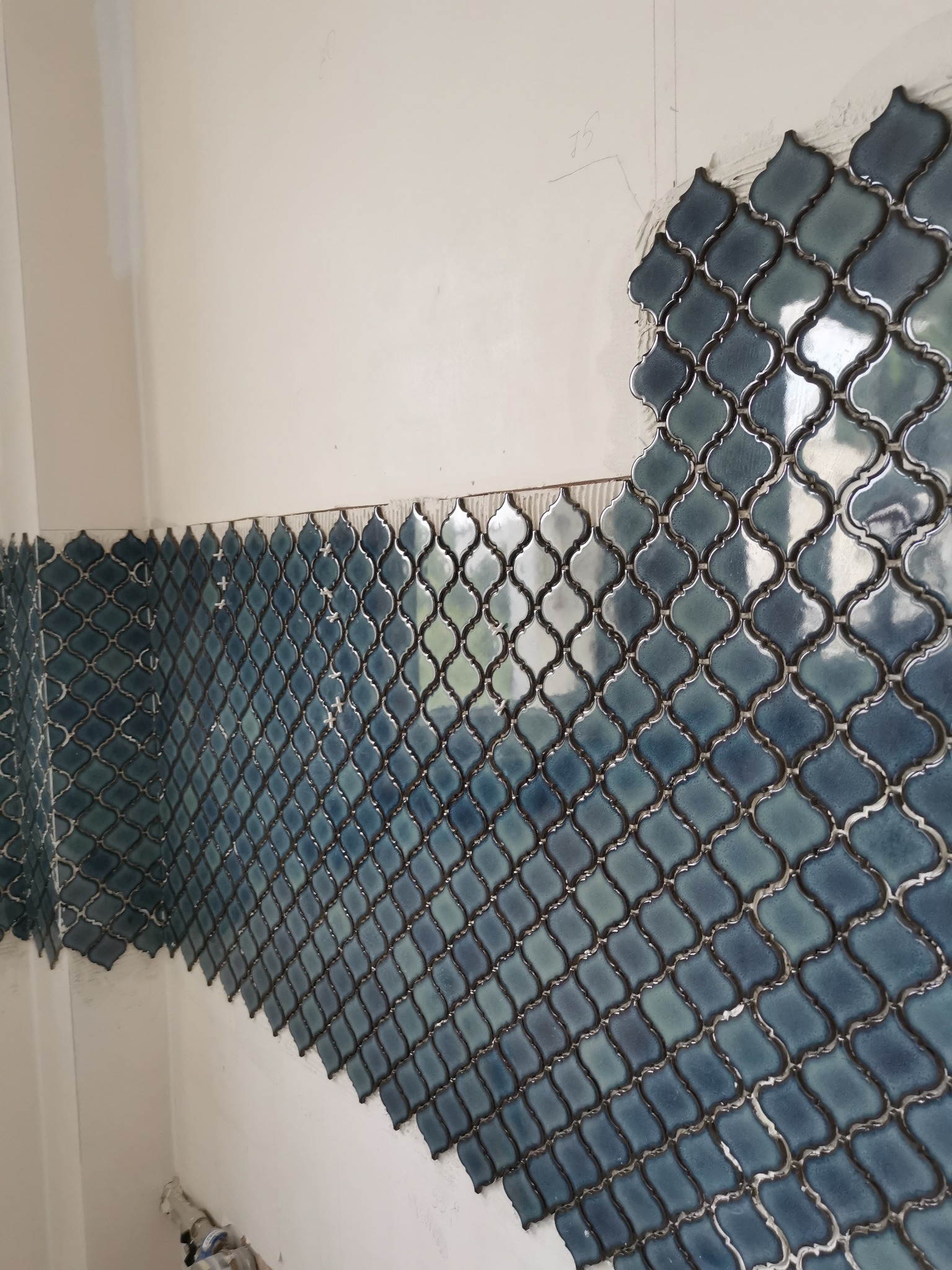 Niebiesko-zielona mozaika w marokańskim stylu układana na ścianie w łazience, widoczne krzyżyki dystansowe i resztki kleju.