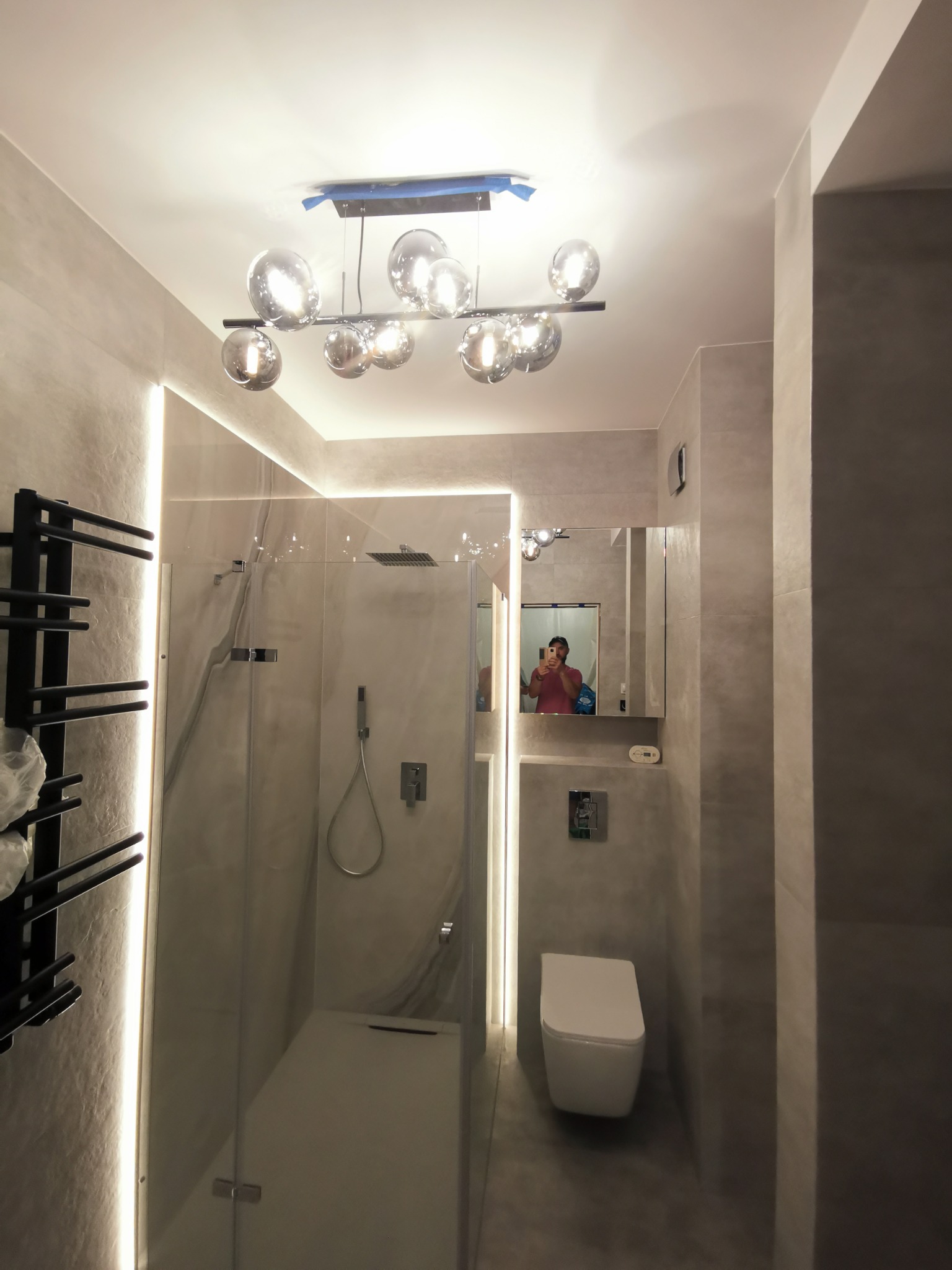 Nowoczesna łazienka w odcieniach szarości z kabiną prysznicową typu walk-in, podświetleniem LED wzdłuż ścian i designerską lampą sufitową z szklanymi kulami.