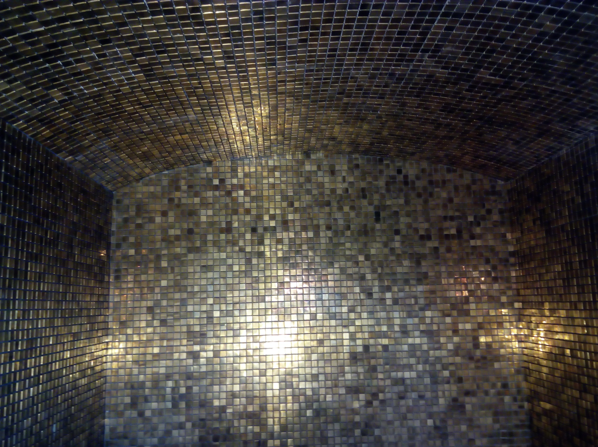 Wnętrze wnęki wyłożone drobną, błyszczącą, złotą mozaiką z wyraźnym odbiciem światła.