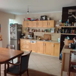 Jasna kuchnia po sprzątaniu: drewniane szafki, czyste blaty, lśniąca podłoga z płytek. Widok na stół i krzesła. Napis 'Po' sugeruje efekt końcowy usługi.