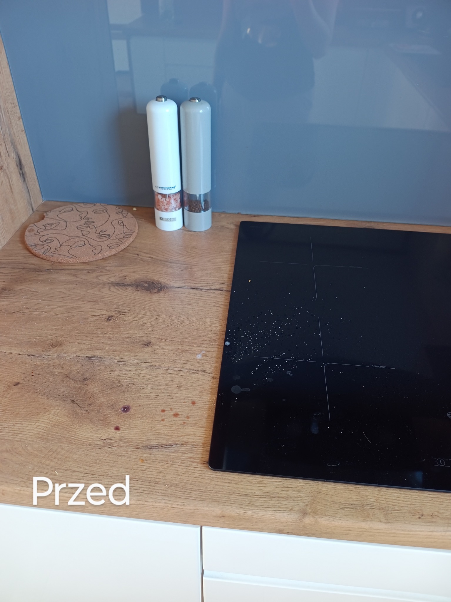 Kuchenny blat w Manowie przed sprzątaniem, z widocznymi plamami i zabrudzeniami obok płyty indukcyjnej, z napisem 'Przed'.