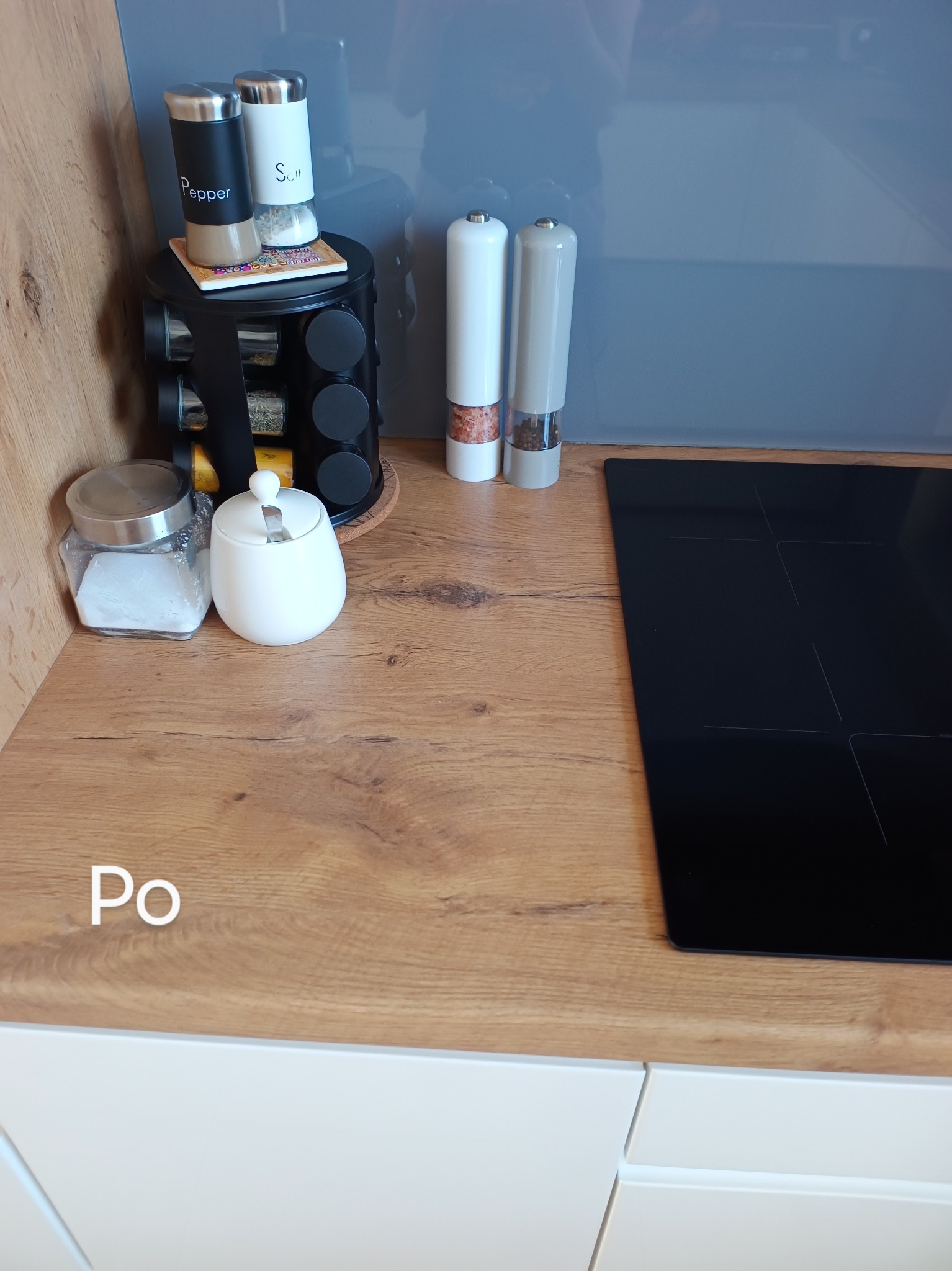 Uporządkowany blat kuchenny z drewnopodobnym wykończeniem po sprzątaniu, widoczne przyprawy, cukiernica i płyta indukcyjna.