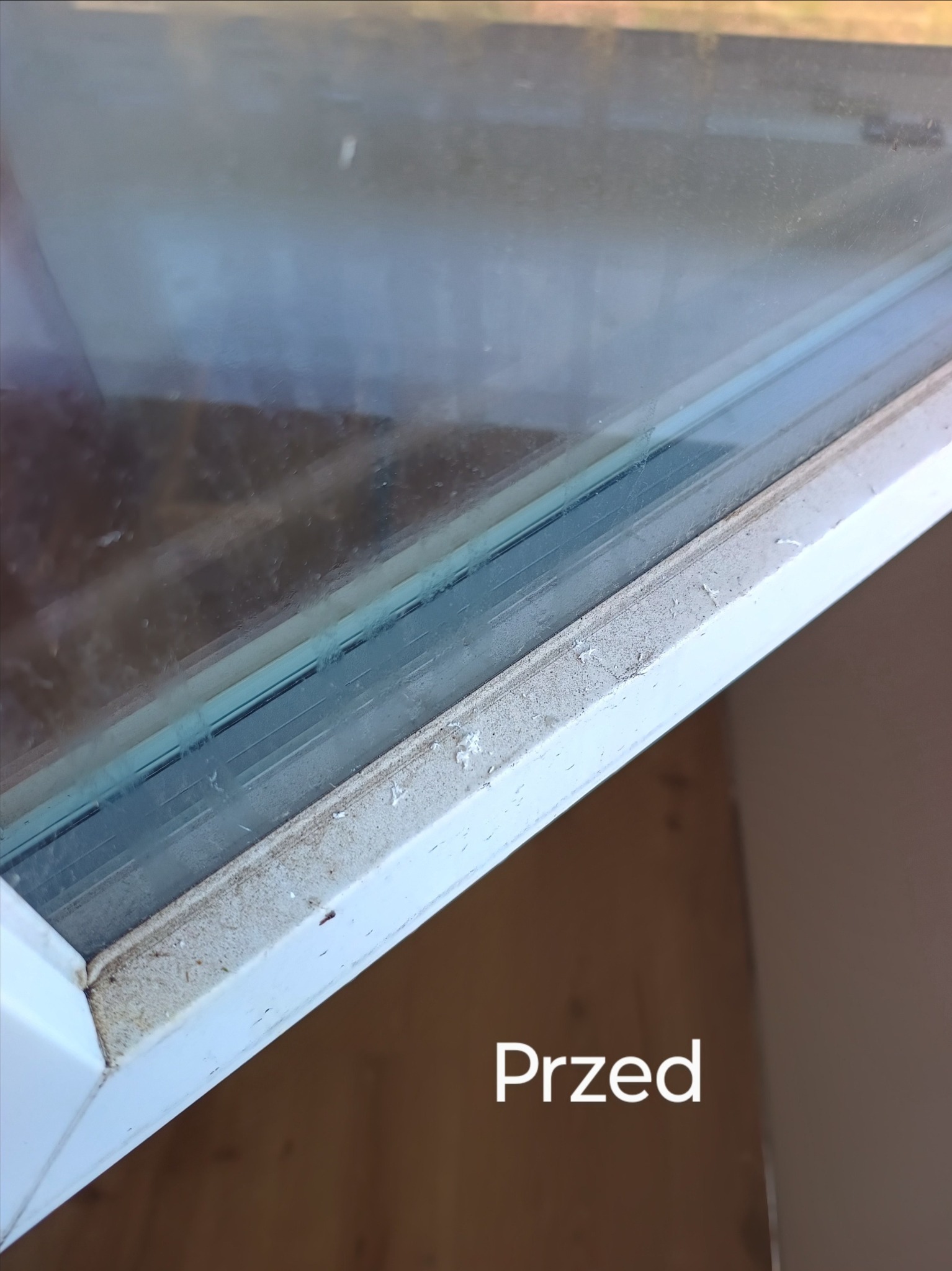 Brudne okno z widocznym osadem i kurzem na ramie, przedstawione w zbliżeniu z napisem 'Przed' - przykład stanu przed czyszczeniem.
