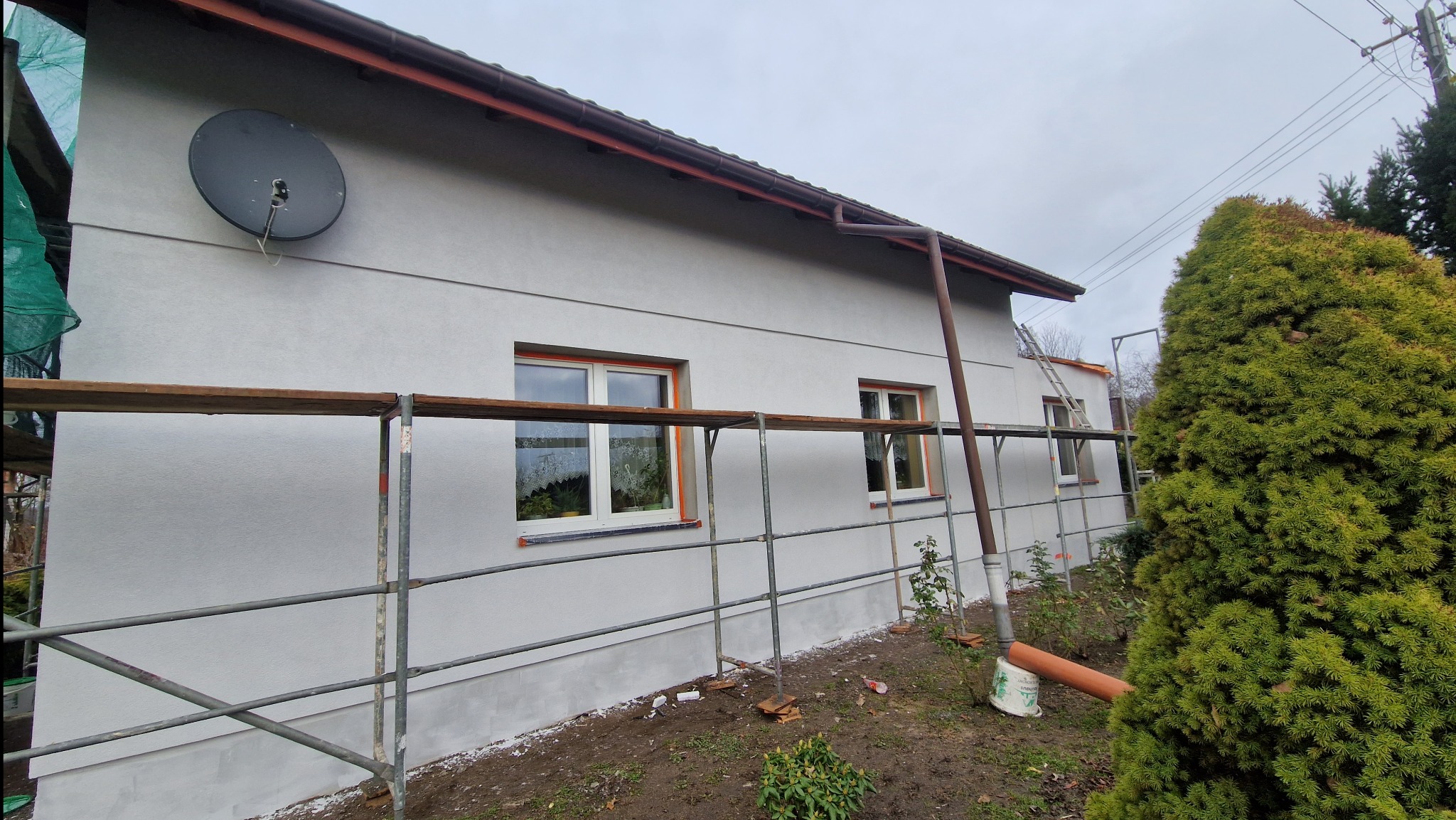 Elewacja domu jednorodzinnego po nałożeniu jasnoszarej gładzi, widoczne rusztowania i antena satelitarna na ścianie
