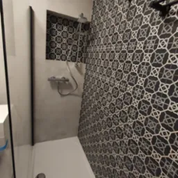 Nowoczesna kabina prysznicowa z geometryczną czarno-białą mozaiką na ścianie, szara wnęka z deszczownicą i baterią, oraz czarne akcenty na ramie kabiny i wieszaku na ręczniki.