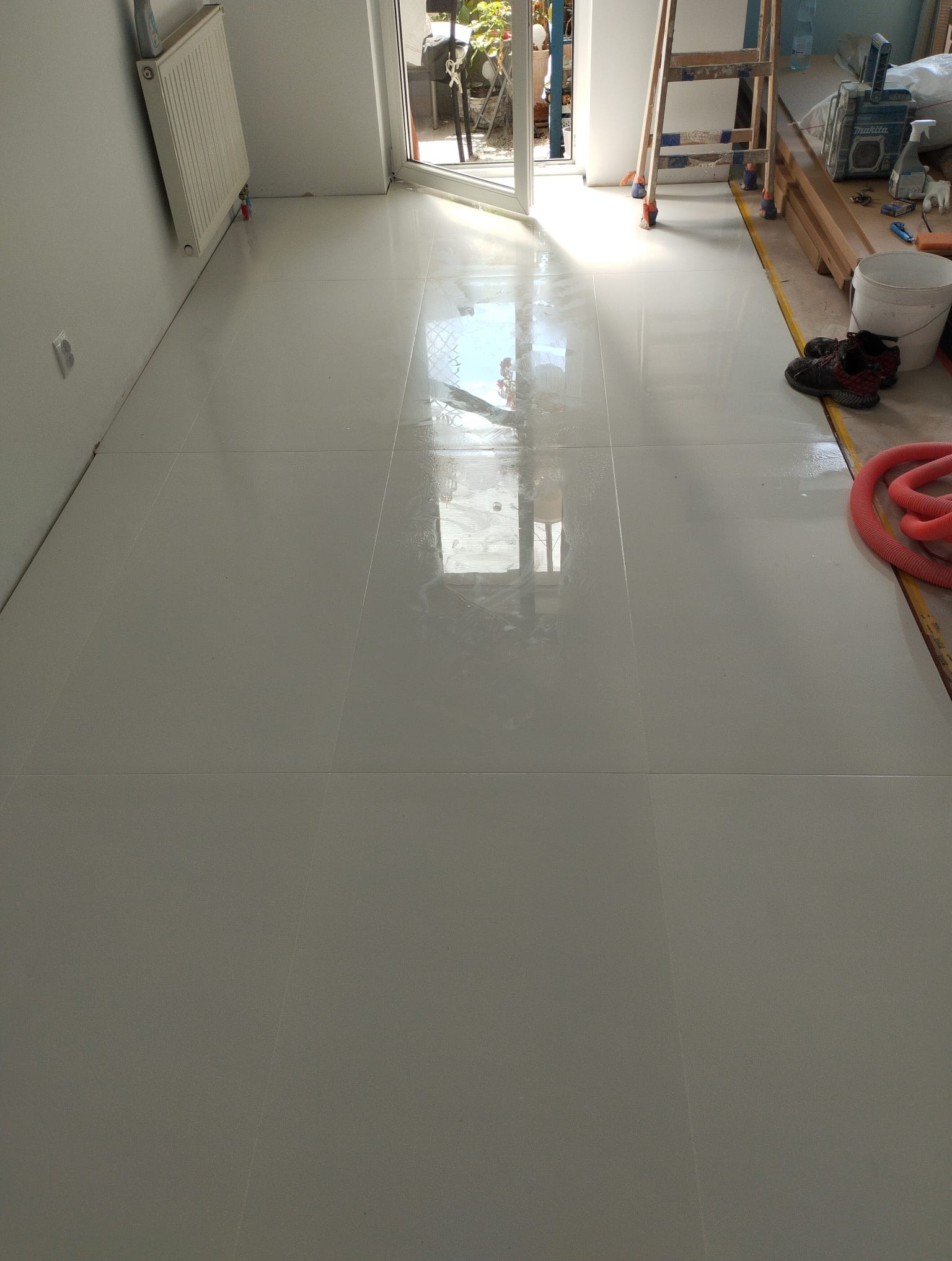 Nowo położone, błyszczące, jasne płytki podłogowe w trakcie prac wykończeniowych w Krakowie, z widocznymi narzędziami i akcesoriami glazurniczymi, drabina oparta o ścianę.