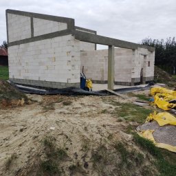 APG CONSTRUCTION SPÓŁKA Z OGRANICZONĄ ODPOWIEDZIALNOŚCIĄ - Wznoszona konstrukcja domu z białych bloczków, widoczne zbrojenia, częściowo wykonane ściany, teren budowy z workami materiałów budowlanych.