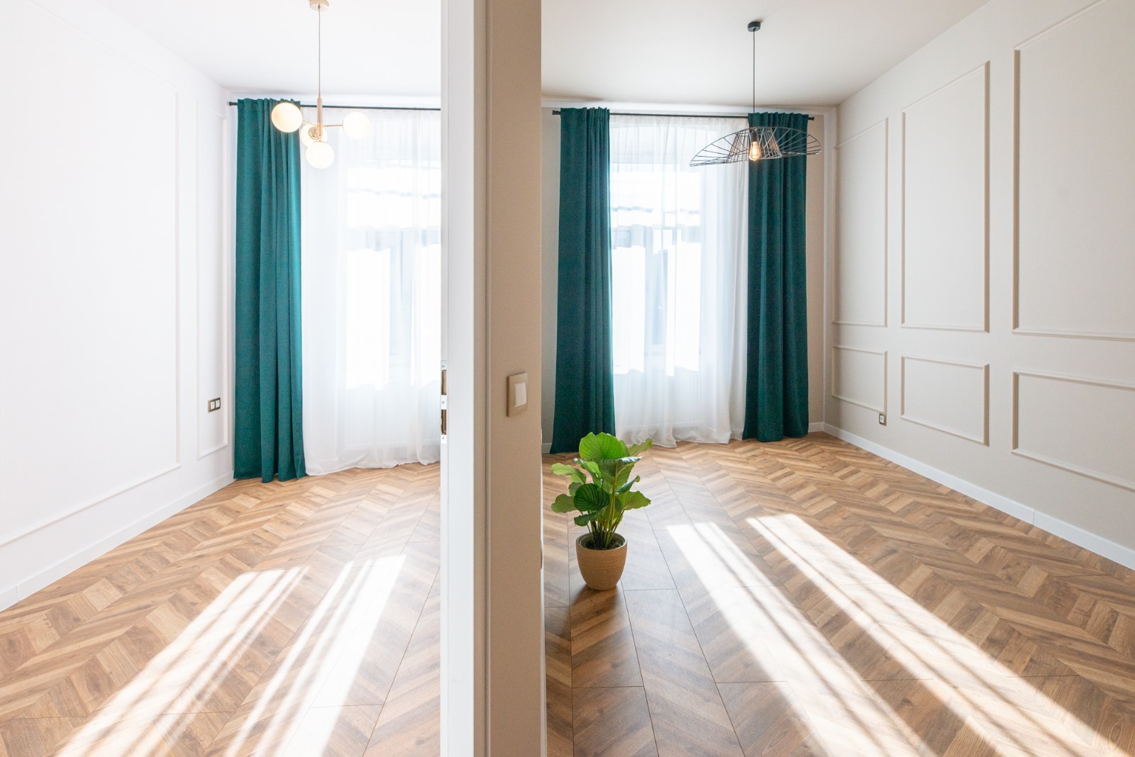Wykończone wnętrze: parkiet w jodełkę, zielone zasłony, białe ściany z dekoracyjnymi listwami, nowoczesne lampy sufitowe i roślina doniczkowa.