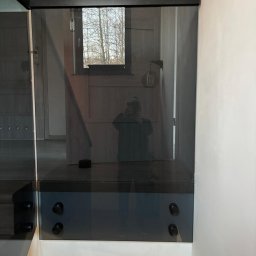 remoglass9 - Szklana balustrada schodowa z czarnymi elementami mocującymi, widoczne odbicie fotografa w szkle.