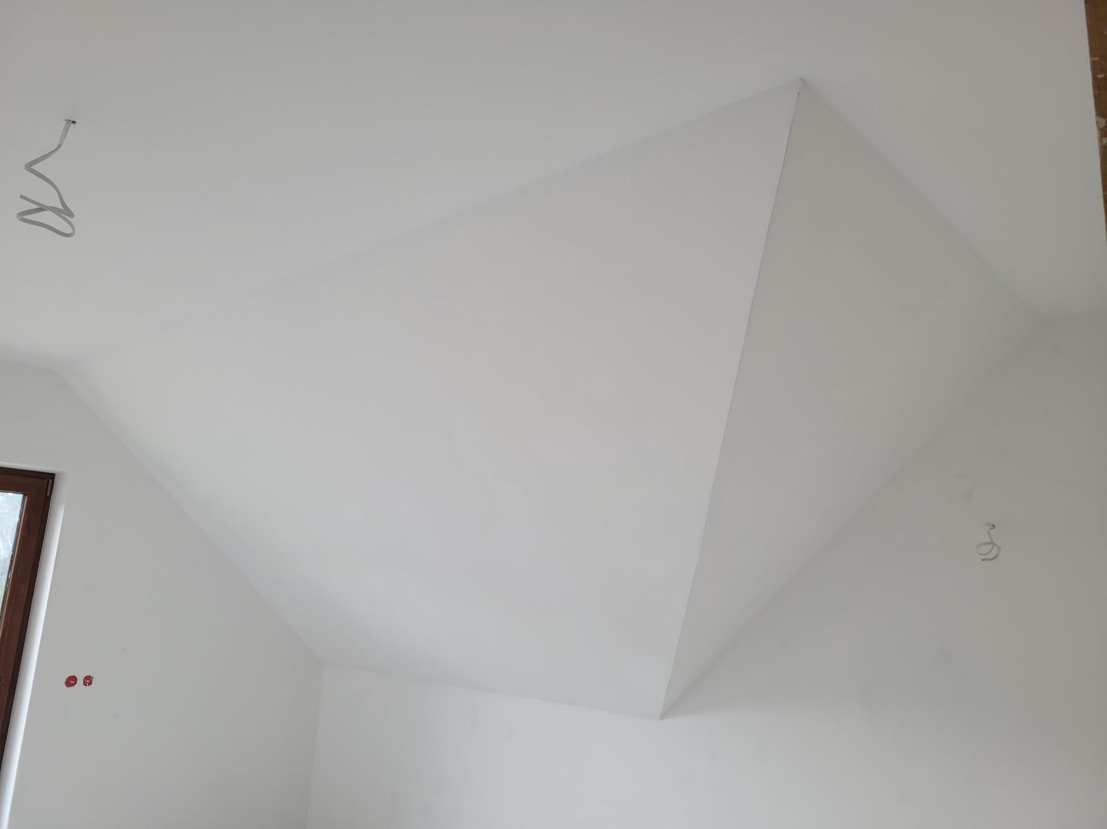 Białe poddasze po remoncie z widocznymi kablami elektrycznymi i fragmentem okna.