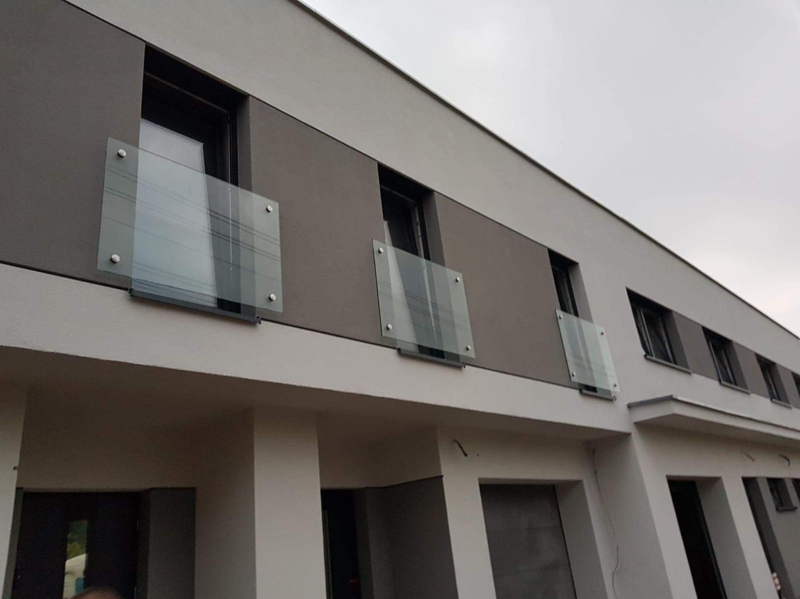 Nowoczesna elewacja budynku z oknami zabezpieczonymi szklanymi balustradami mocowanymi punktowo.