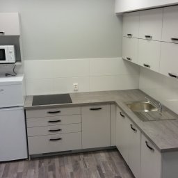 Rystol sp.z oo - Jasna zabudowa kuchenna z szarym blatem i sprzętem AGD w Toruniu. Minimalistyczny design, widok na szafki górne i dolne, zlew oraz płytę indukcyjną.