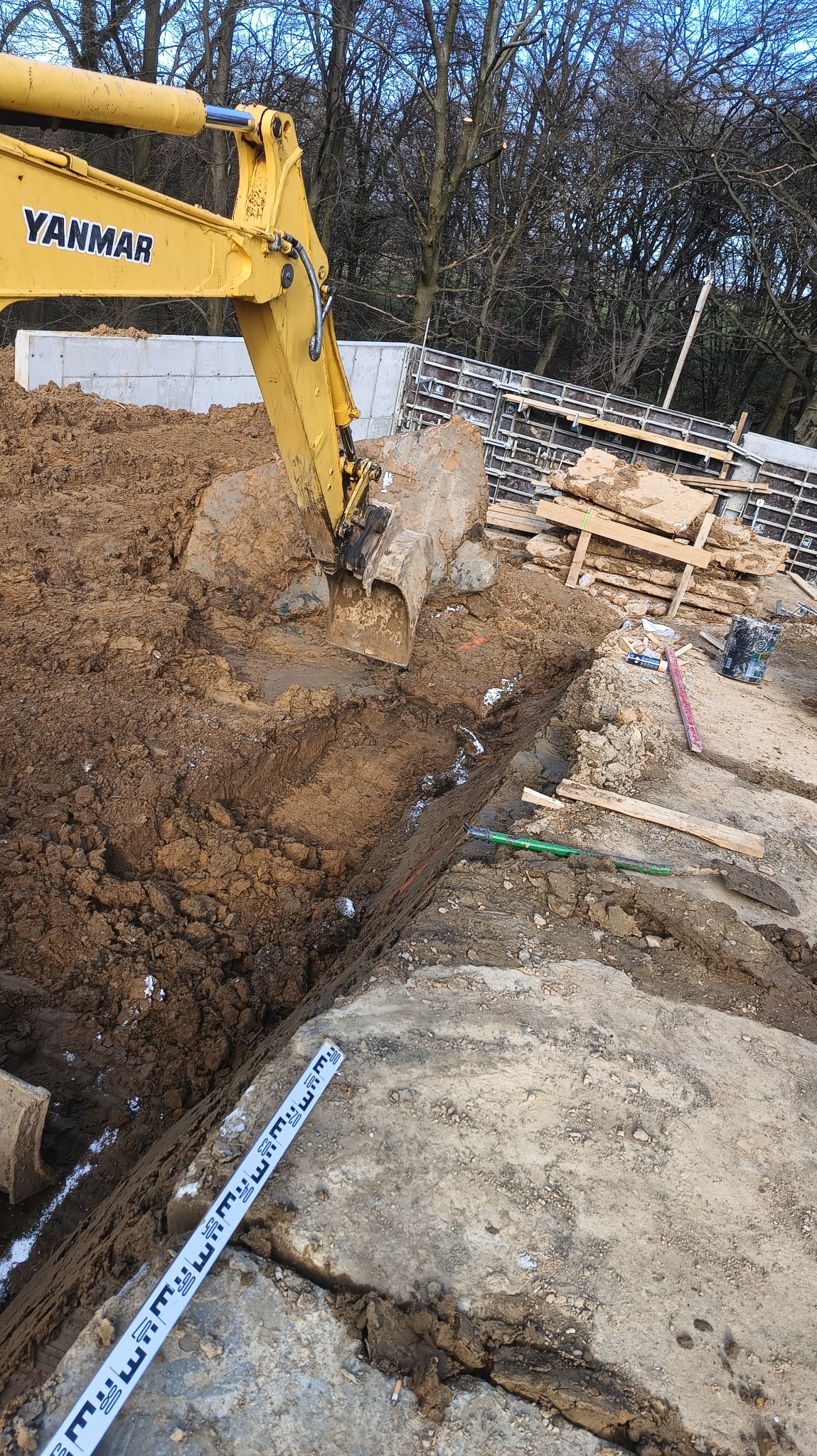 Żółta koparka Yanmar pogłębia wykop pod fundament, widoczne szalunki i poziomica