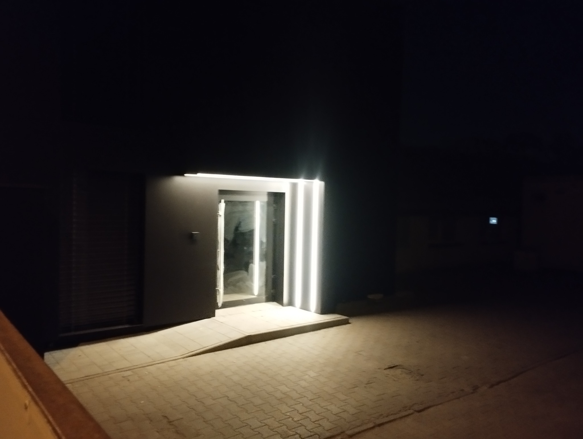 Nowoczesne wejście do budynku z otwartymi drzwiami i oświetleniem LED, widoczne z zewnątrz w słabym oświetleniu nocnym.