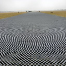 PRZEDSIĘBIORSTWO WIELOBRANŻOWE WIKTOR BORZYSZKOWSKI - Rozległa powierzchnia wyłożona szarymi płytami ażurowymi Terra-Grid E® 35, widok z perspektywy ziemi, w tle słabo widoczne maszyny budowlane i drzewa, pochmurne niebo.