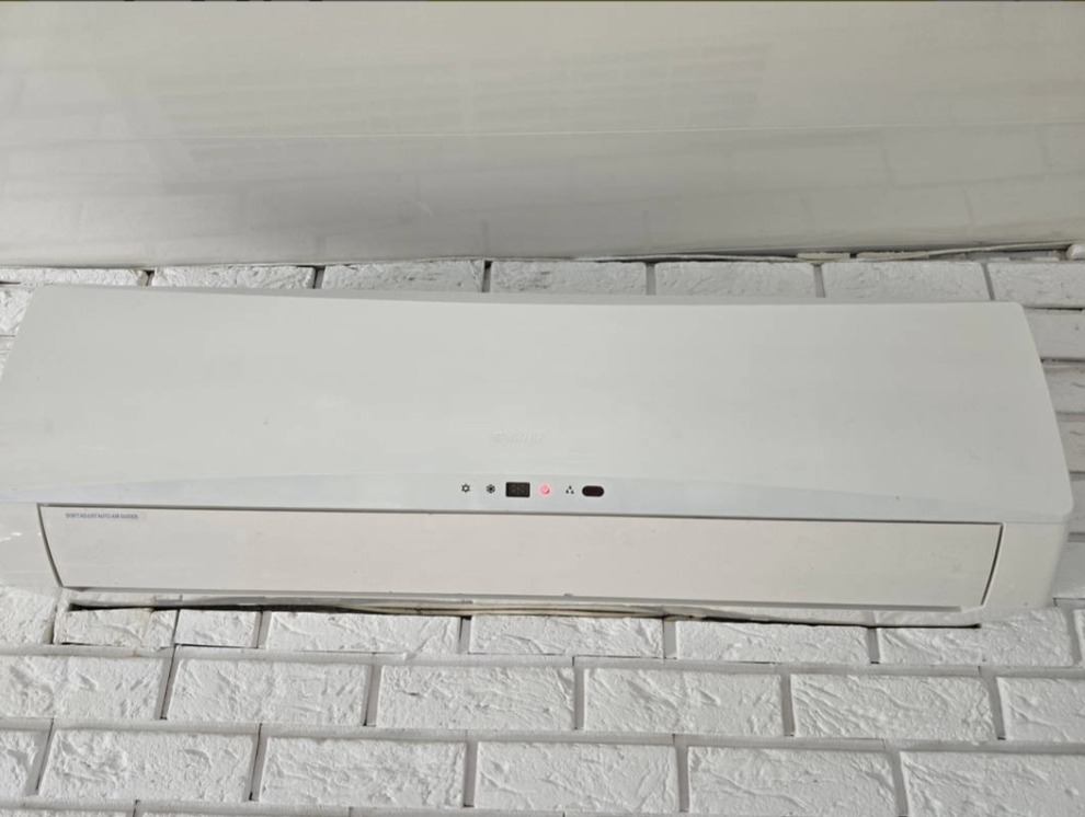 Biały klimatyzator zamontowany na ścianie z białej cegły dekoracyjnej, widoczne diody kontrolne.