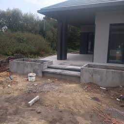 Mateusz Raduj - Wykonywanie fundamentów pod taras domu jednorodzinnego w Księżpolu, widoczne betonowe ściany fundamentowe i schody wejściowe, teren wokół w trakcie prac ziemnych.