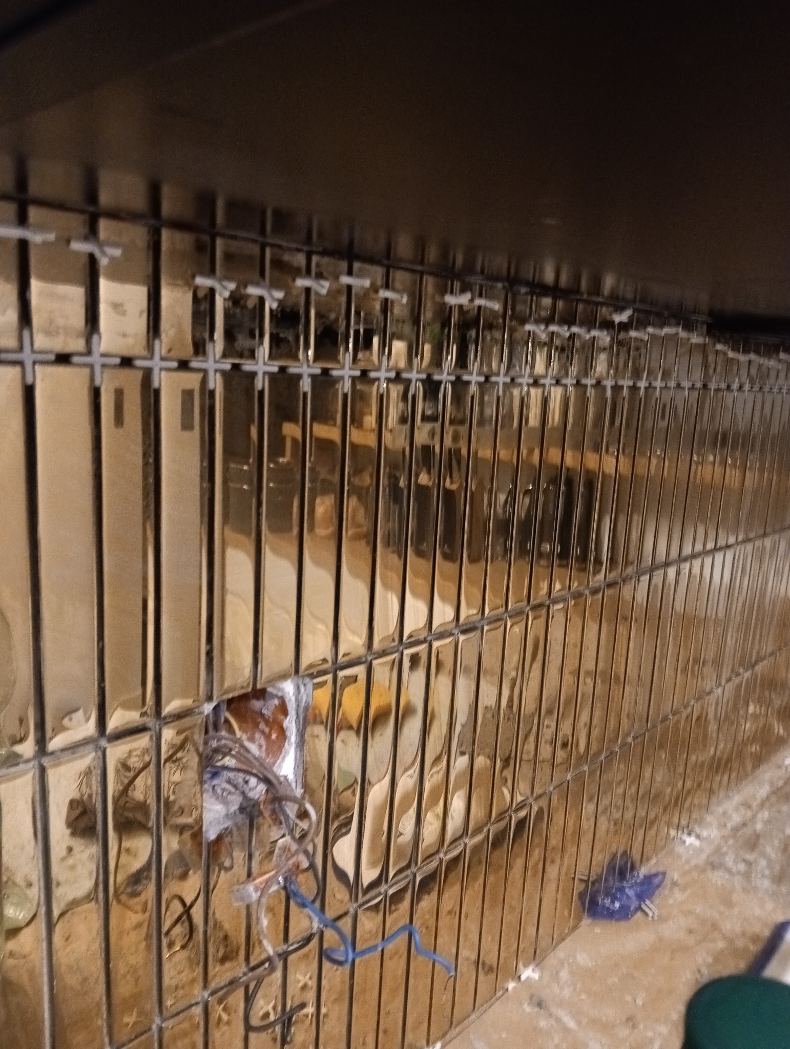 Montaż błyszczących, złotych płytek na ścianie z widoczną puszką elektryczną i wystającymi przewodami, etap prac wykończeniowych.