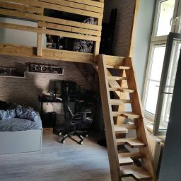 Jonasz Henszel - Drewniana antresola z drabinką w pokoju, widok na biurko i łóżko, naturalne drewno, schody z wycięciami na stopy.