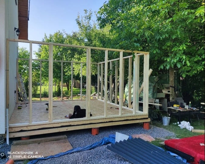 Konstrukcja drewniana w trakcie budowy, widok z zewnątrz, z narzędziami i materiałami budowlanymi w tle.