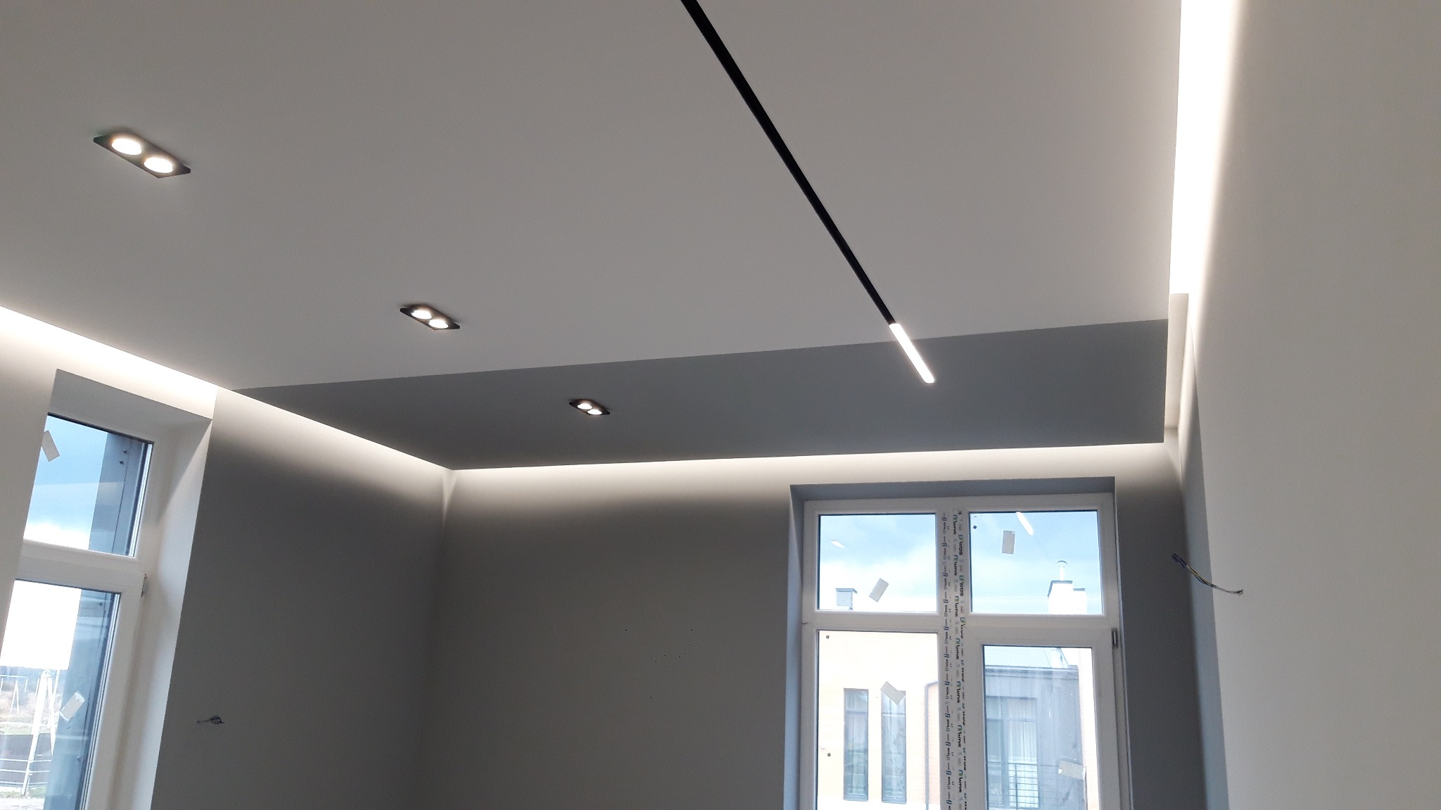 Nowoczesne oświetlenie sufitowe w szarej tonacji z lampami punktowymi i liniowymi LED, widok na dwa okna, minimalistyczny design wnętrza.