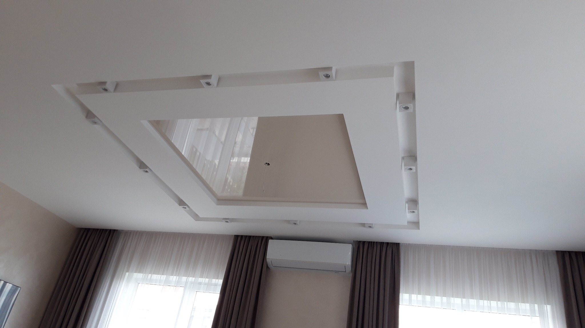 Biały sufit podwieszany z oświetleniem punktowym w pokoju z zasłonami i klimatyzatorem, widziany pod kątem. Nowoczesne wykończenie wnętrza.