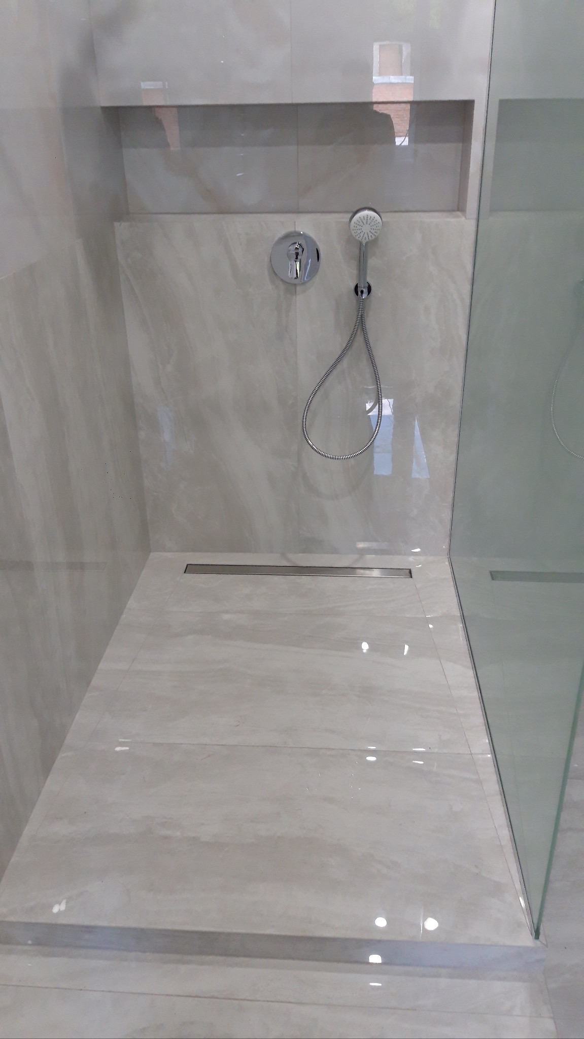 Elegancka kabina prysznicowa z beżowymi płytkami imitującymi marmur, wyposażona w deszczownicę i odpływ liniowy. W tle wnęka ścienna.