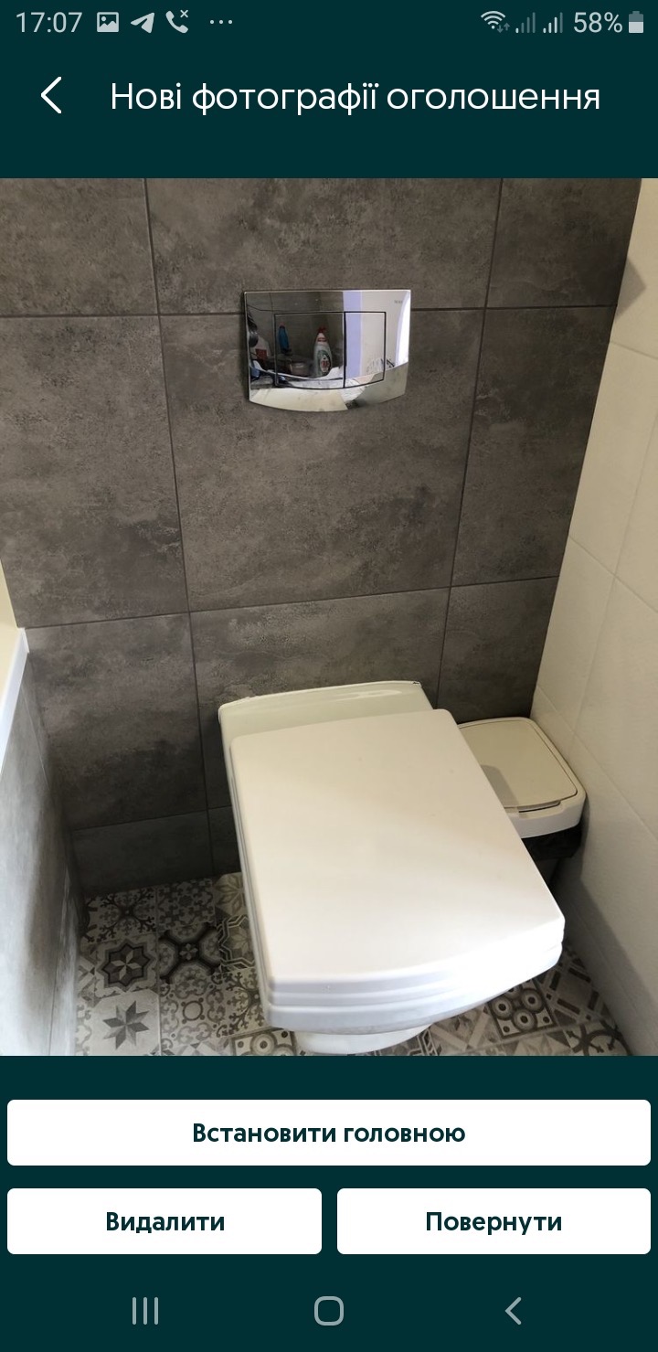 Nowoczesna toaleta z zabudowaną spłuczką na tle szarych płytek. Wzory na podłodze dodają charakteru. Minimalistyczny design.