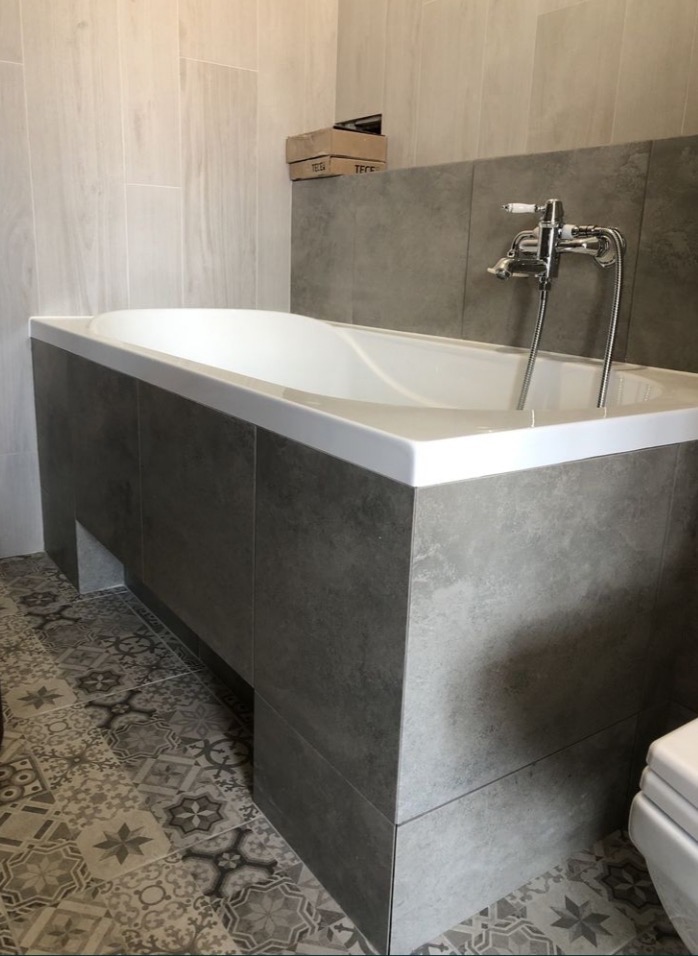 Wykończona łazienka w Szczecinie: obudowana wanna z szarą glazurą, mozaika na podłodze i chromowana bateria. Estetyczne wykończenie.