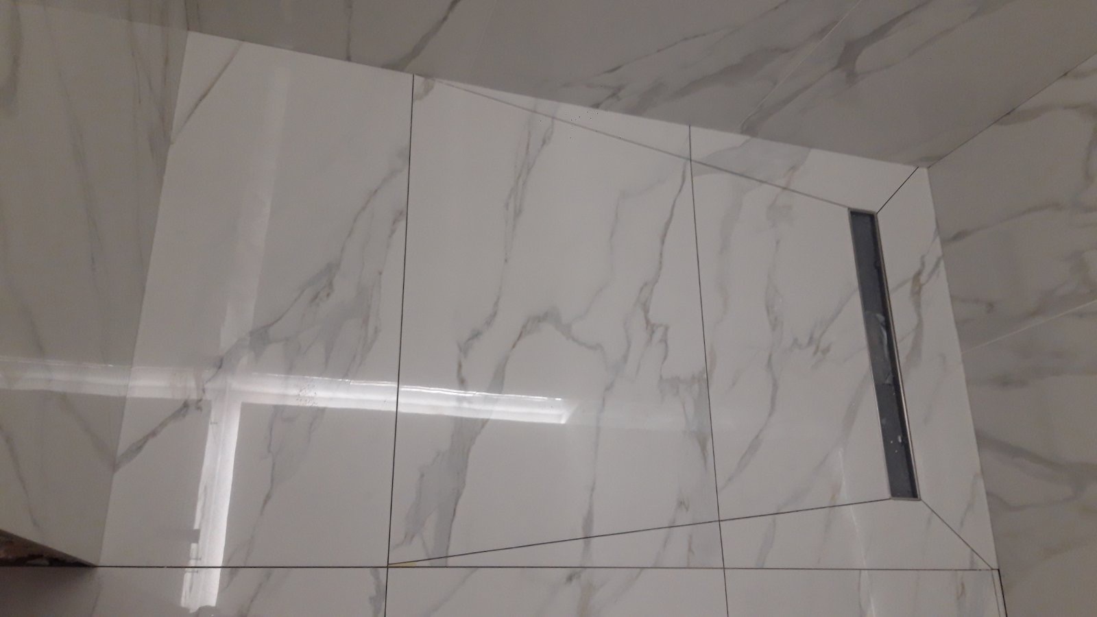 Białe, marmurowe płytki w łazience z odpływem liniowym. Minimalistyczny design, precyzyjne fugi. Wykończenie pod kątem, widok z góry.