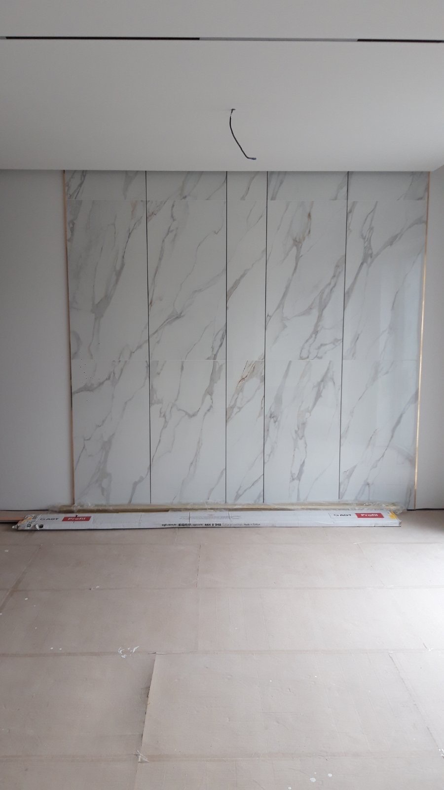 Ściana wykończona panelami imitującymi marmur w Szczecinie. Widoczne listwy przypodłogowe w opakowaniu. Podłoga przygotowana do dalszych prac wykończeniowych.