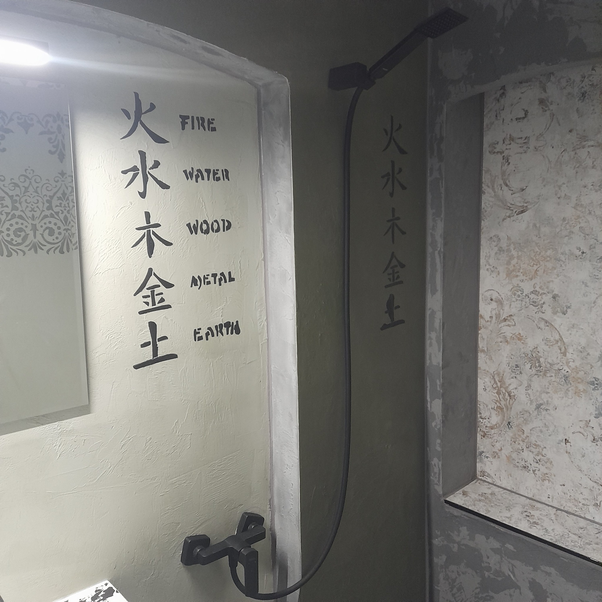 Nowoczesna łazienka z kabiną prysznicową typu walk-in, ściany zdobione motywami inspirowanymi pięcioma żywiołami w języku angielskim i chińskim, czarna bateria natryskowa.