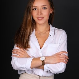 Martyna Mierzicka - MARLENS Fotografia - Portret uśmiechniętej kobiety w białej koszuli i beżowych spodniach na ciemnym tle, z założonymi rękami, złotym zegarkiem i naszyjnikiem z księżycem