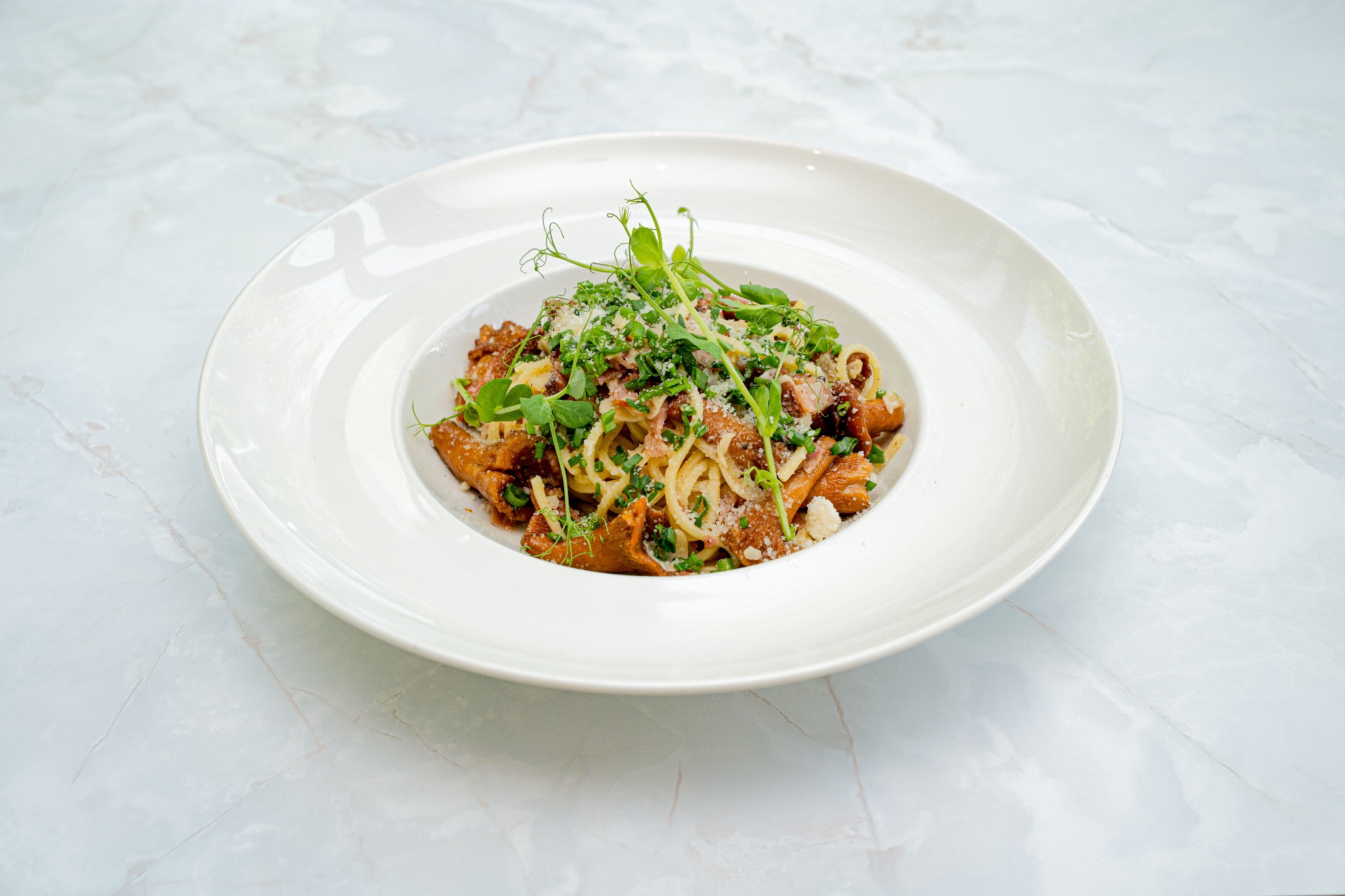 Apetyczne danie: spaghetti z kurkami, parmezanem i świeżymi ziołami, podane na białym talerzu na marmurowym blacie. Ujęcie z góry, ostre światło.