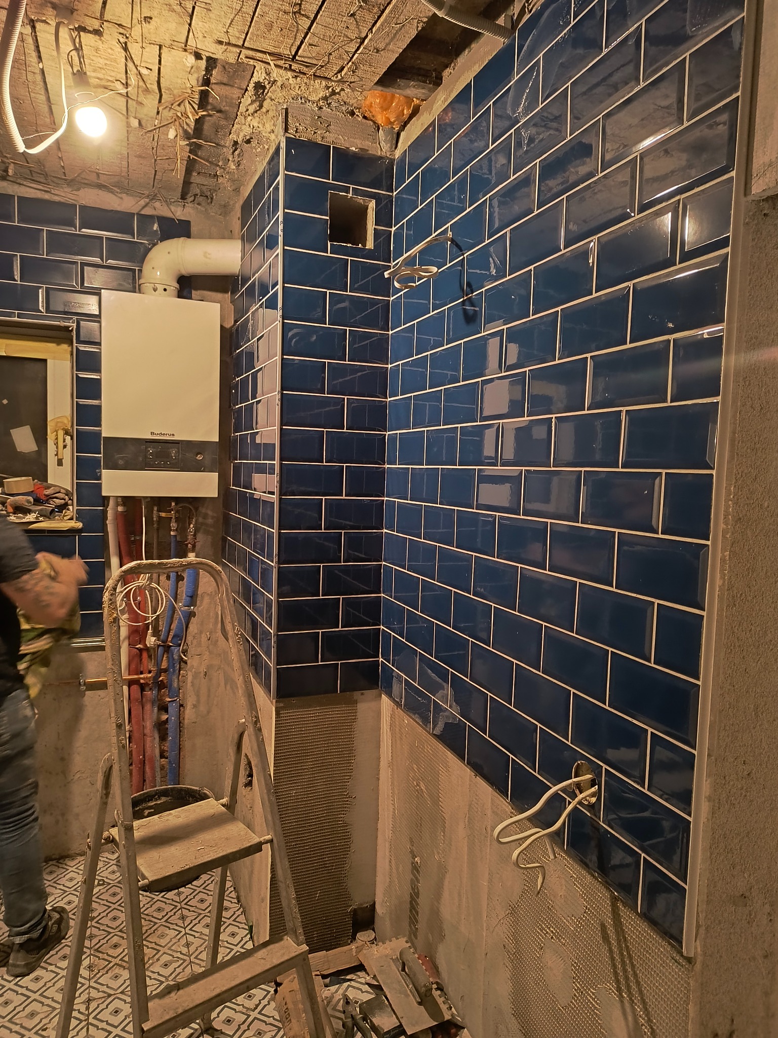 Montaż ciemnoniebieskich płytek typu metro w łazience w Lęborku, widoczny piec gazowy, drabina i instalacja wodna, surowy stan wykończenia.