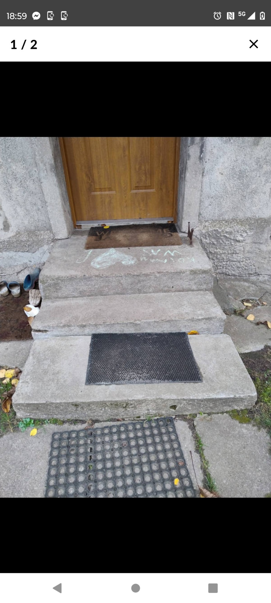 Zewnętrzne schody betonowe prowadzące do brązowych drzwi wejściowych, z wycieraczkami na każdym stopniu i dziecięcymi rysunkami kredą na górnym stopniu.